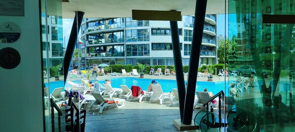 Un edificio moderno con zona de piscina, sillones reclinables y sombrillas.