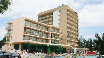 Un hotel de varios pisos con balcones, piscina y sillones de descanso.