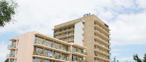 A multi-story hotel with balconies, a swimming pool, and lounge chairs.