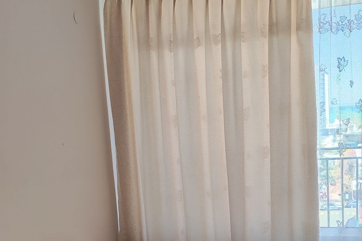 Una cama bien hecha con una colcha estampada, una ventana con cortinas y vistas a un balcón.