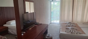 Quarto de hotel com uma cama, televisão, secretária de madeira e varanda com cortinas.