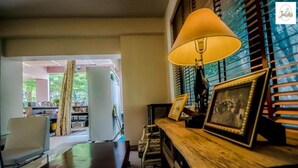 Une pièce avec une table en bois, une lampe et un tableau encadré. On y trouve une chaise et une fenêtre avec des stores.