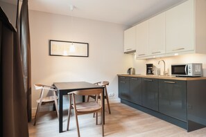 A modern kitchen with dark cabinets, a wooden dining table, and a hanging light fixture. - Exclusive Apartments (Wroclaw)