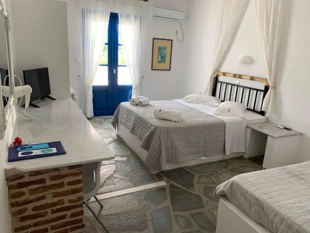 A bedroom with two beds, a desk, a chair, a TV, and a window with curtains.