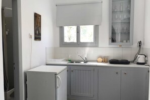 Uma cozinha compacta com janela, pia, pequena geladeira e armário com copos.