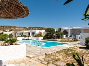 A pool area with a clear blue sky, white buildings, and a view of a hilly landscape. - Naoussa Hotel (Paros)