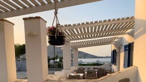 A covered outdoor seating area with stone walls and a view of the sea. - Naoussa Hotel (Paros)