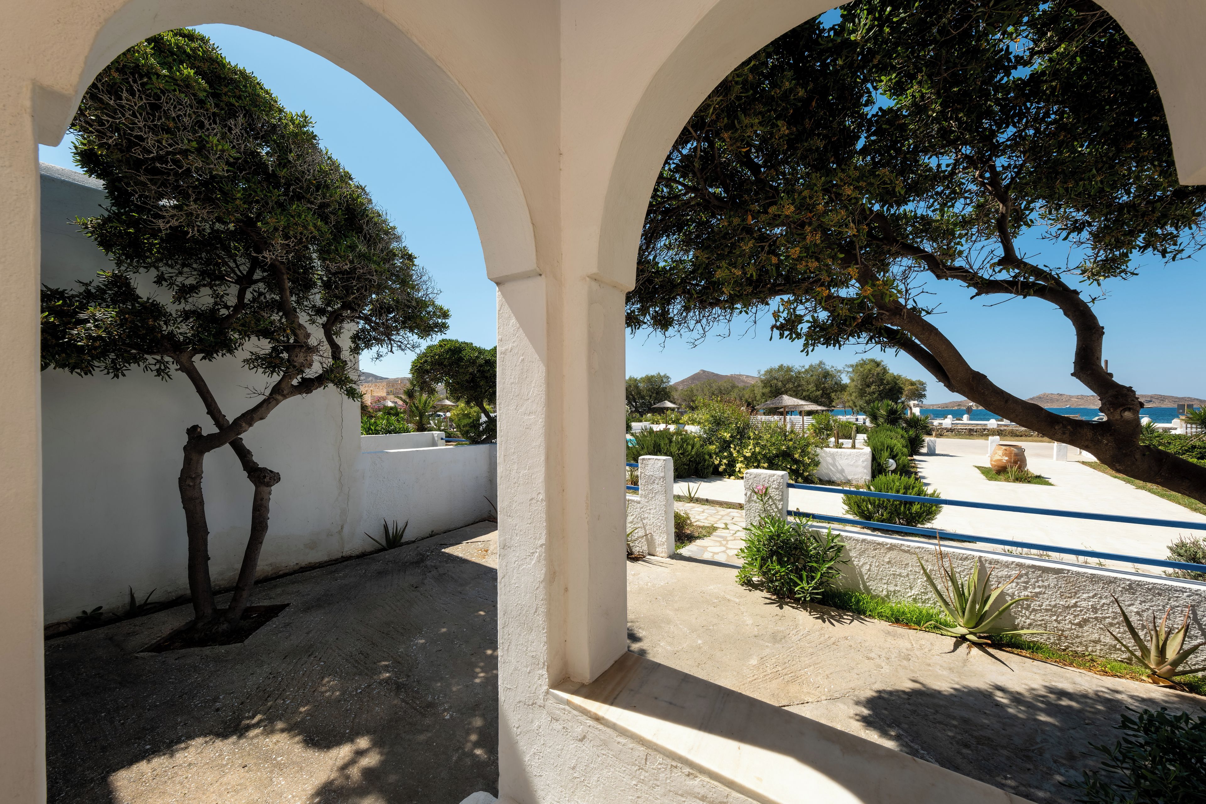 An outdoor area with white arches, a tree, and a view of the sea.