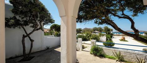 An outdoor area with white arches, a tree, and a view of the sea.
