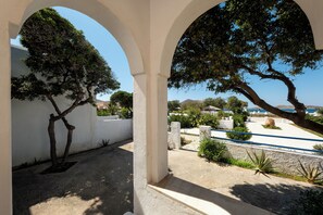 An outdoor area with white arches, a tree, and a view of the sea. - Naoussa Hotel (Paros)