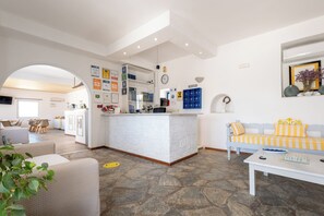 Ampla sala de estar com um balcão de recepção branco, um sofá com listras amarelas e piso com padrão de pedra.