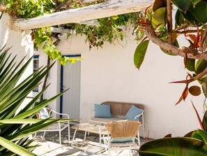 A patio with a white wall, a wooden bench, a wicker chair, and a door. - Naoussa Hotel (Paros)