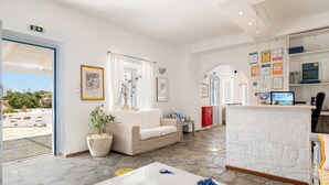 A hotel lobby with a white sofa, a reception desk, and a large window. - Naoussa Hotel (Paros)
