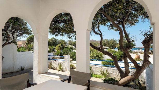 An outdoor seating area with white tables and chairs, surrounded by white arches and trees. - Naoussa Hotel (Paros)