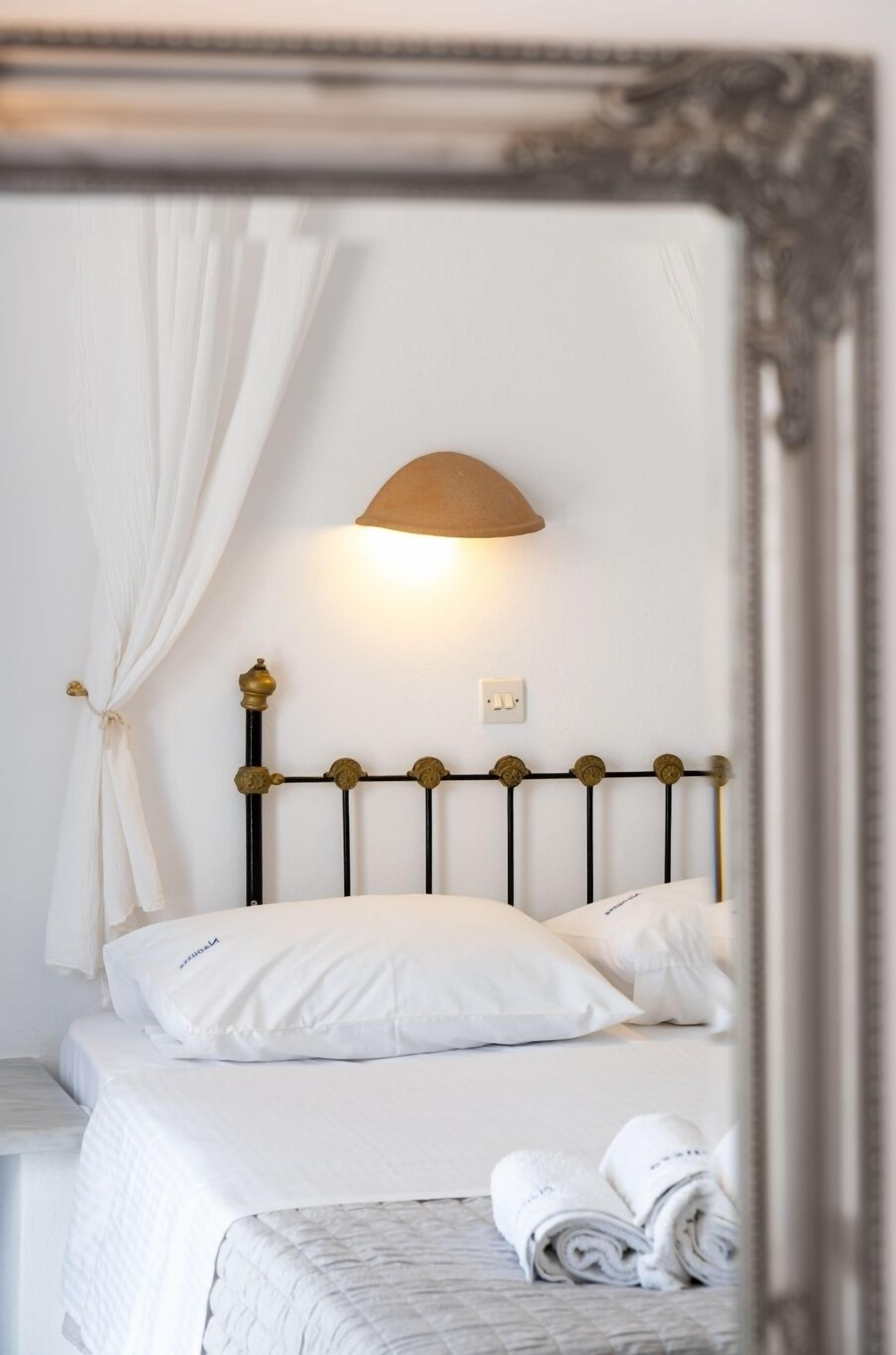 A bed with a headboard, a wall-mounted light, and a mirror reflecting part of the room.