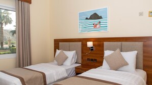 Ein Hotelzimmer mit zwei Betten, einem Holzkopfteil, einem Nachttisch, einer Lampe und einem Gemälde mit einer Berg- und Wasserausicht.
