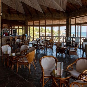 A spacious indoor area with wicker furniture, a bar, and large windows overlooking a beach. - Sandy Beach Hotel Resort (Al Aqah)