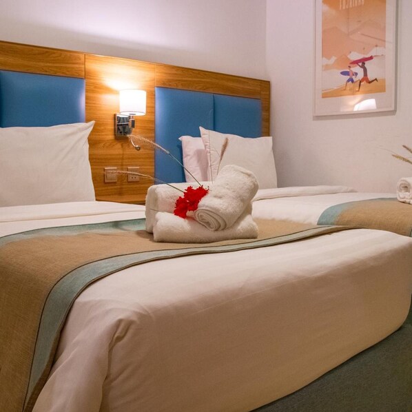 A hotel room with two beds, a wooden headboard, a wall-mounted lamp, and a framed picture. - Sandy Beach Hotel Resort (Al Aqah)