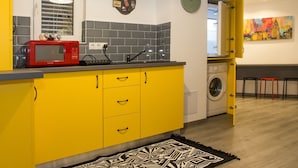 A compact kitchen with yellow cabinets, a red microwave, a clock, and a washing machine. - Redbed Self-catering Apartments (Bucharest)