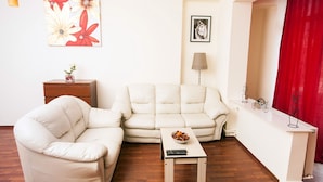 A living room with a sofa, a small table, a lamp, and a red curtain. - Redbed Self-catering Apartments (Bucharest)