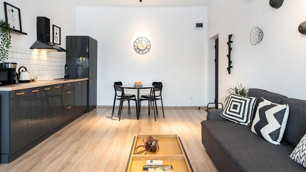 A modern kitchen with black cabinets, a wooden countertop, and a dining area with a table and chairs. - Redbed Self-catering Apartments (Bucharest)