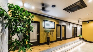 A hotel hallway with a wooden floor, a reception desk, a mounted TV, and a plant. - H Daimyo (Fukuoka)