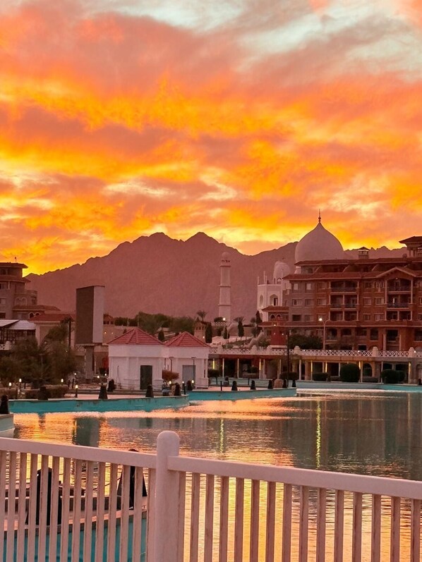 A hotel with a pool, a mountain backdrop, and a sunset sky.