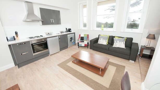 A modern apartment with a kitchen, dining area, and living room. It includes a built-in oven, a washing machine, and a sofa with cushions. - Coldeast Mansion (Southampton)
