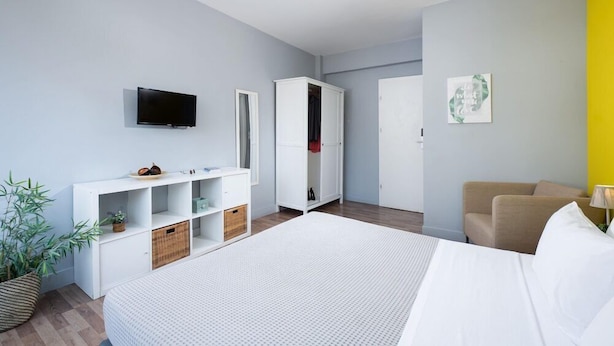 A modern hotel room with a large bed, a TV mounted on the wall, a wardrobe, and a seating area with a lamp. - Xenofontos Inn by Livin Urbban (Athens)