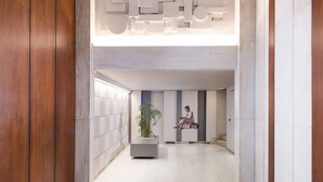 A modern hallway with a wooden panel wall, a large potted plant, and a wall-mounted artwork of a seated figure. - Xenofontos Inn by Livin Urbban (Athens)