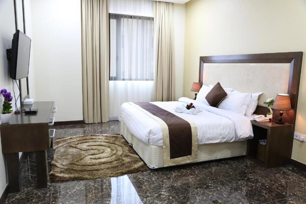 A hotel room with a bed, a desk, a TV, a window with curtains, and a rug.