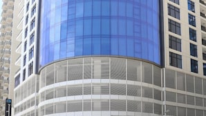 Un bâtiment moderne doté d’une façade en verre incurvée et d’une partie inférieure blanche ornée de lignes horizontales.