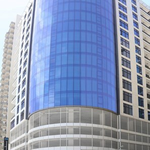 Um edifício moderno com fachada de vidro curvo e uma seção inferior branca com linhas horizontais.