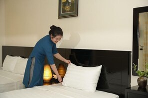 Una persona ajusta un almohadón blanco en una cama con cabecera negra en una habitación de hotel.