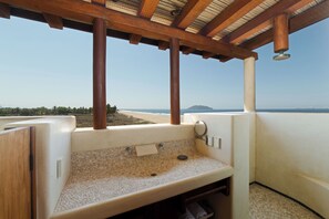 A bathroom with a pebble-tiled sink, wooden pillars, and a view of the beach. - Casa de Olas, Stunning Oceanfront Villa in Las Palmas (Zihuatanejo)