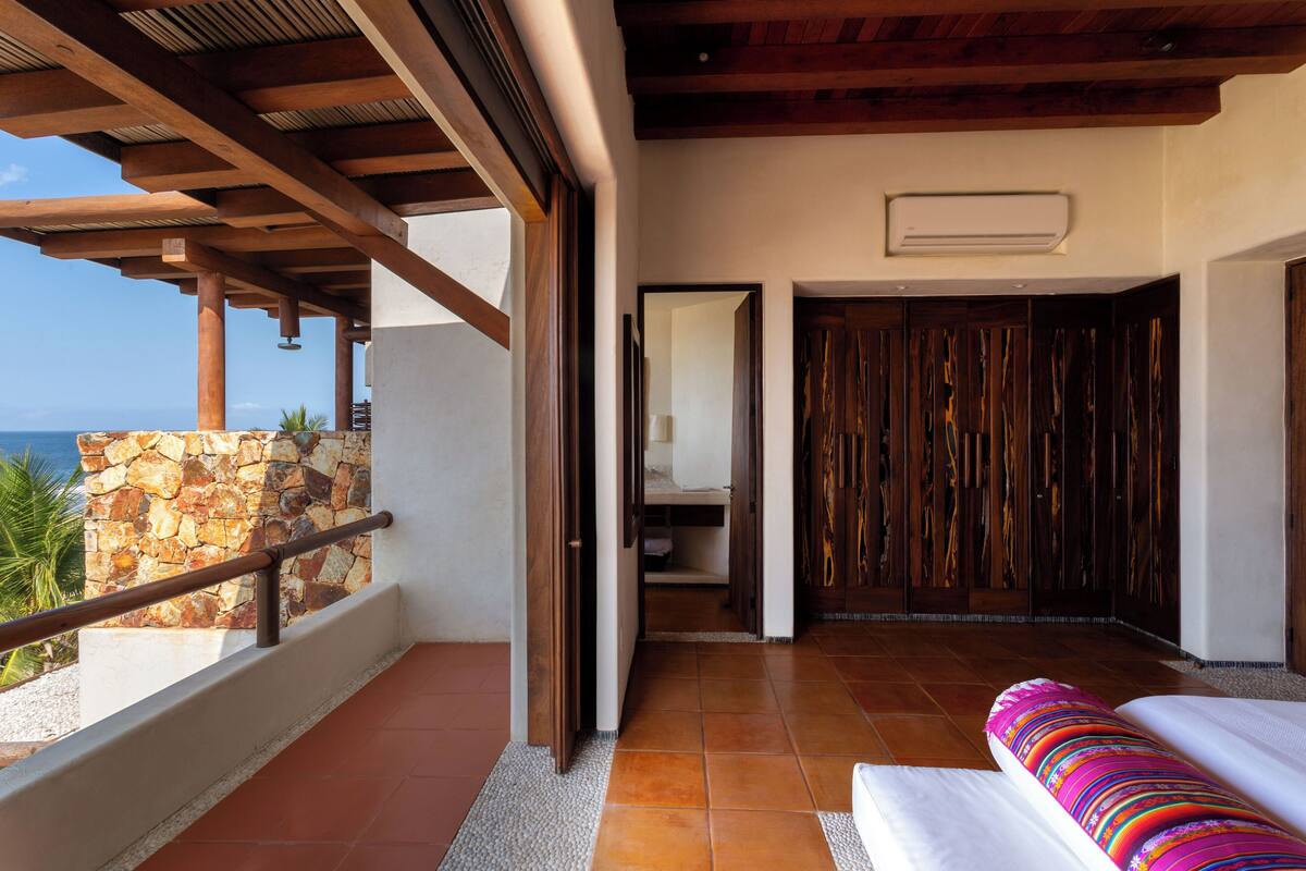 A balcony with a stone wall, a wooden ceiling, and a view of the ocean.