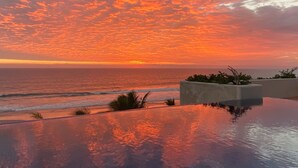 Vista del atardecer sobre el océano con una piscina en primer plano.
