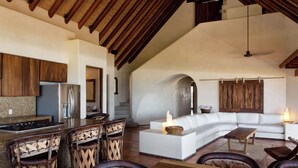 Amplia sala de estar con sofá blanco, mesa de centro de madera y área de cocina con refrigerador y taburetes de bar.