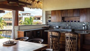 Una cocina con techo de paja, armarios de madera y vistas a palmeras y edificios.