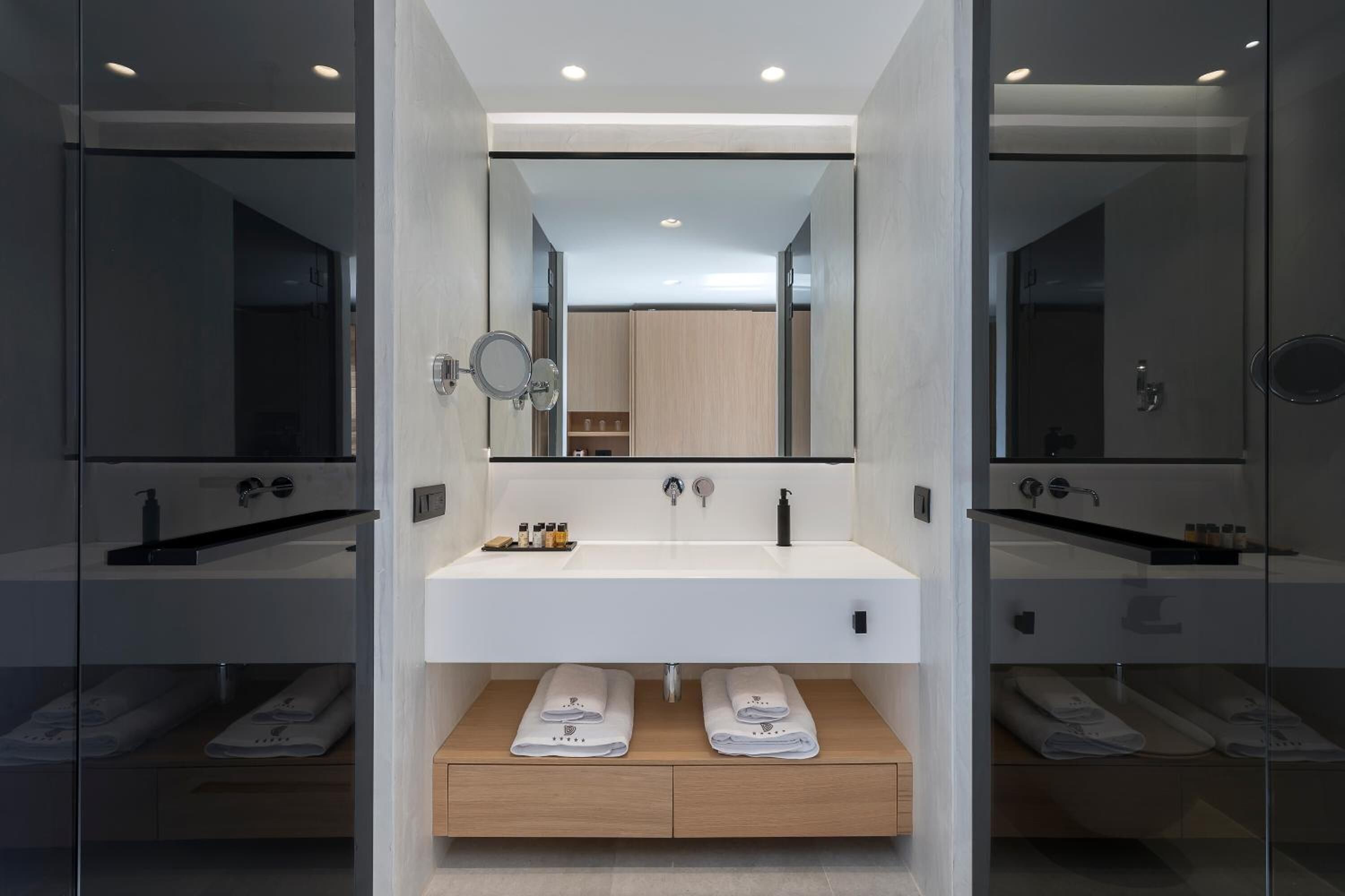 A modern bathroom with a large mirror, white sink, and two towel racks.