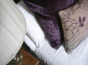A bed with white sheets, a purple pillow, and a floral-patterned pillow.