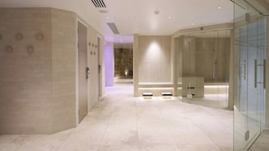 A modern bathroom with a glass shower enclosure, a marble-tiled floor, and a stone wall in the background. - The Fairlawns Hotel And Spa (Walsall)