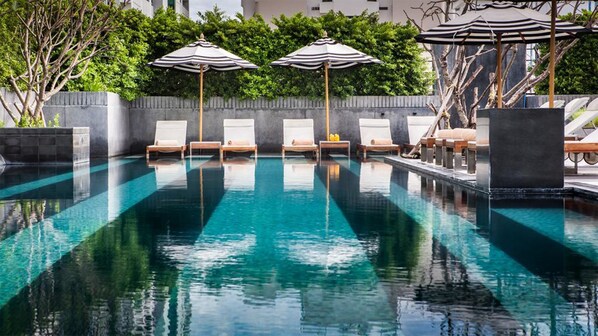 A pool with clear water, surrounded by lounge chairs and striped umbrellas. - Alansea Danang Hotel (Da Nang)
