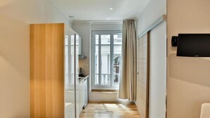 A narrow hallway with wooden flooring, a white door leading to a balcony, and a flat-screen TV mounted on the wall. - Nice Home Studio (Nice)