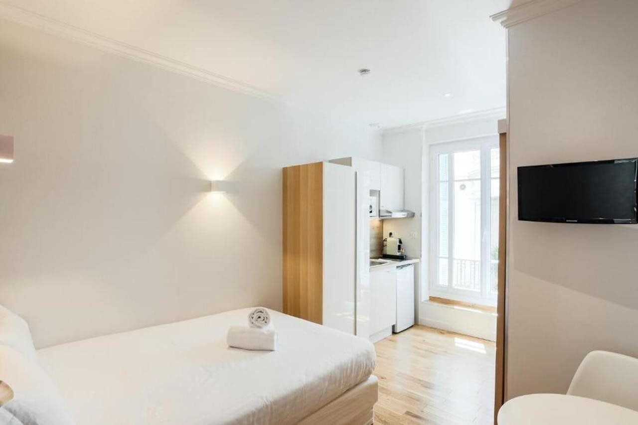 Een moderne hotelkamer met een bed, een televisie, een kitchenette en een balkon.