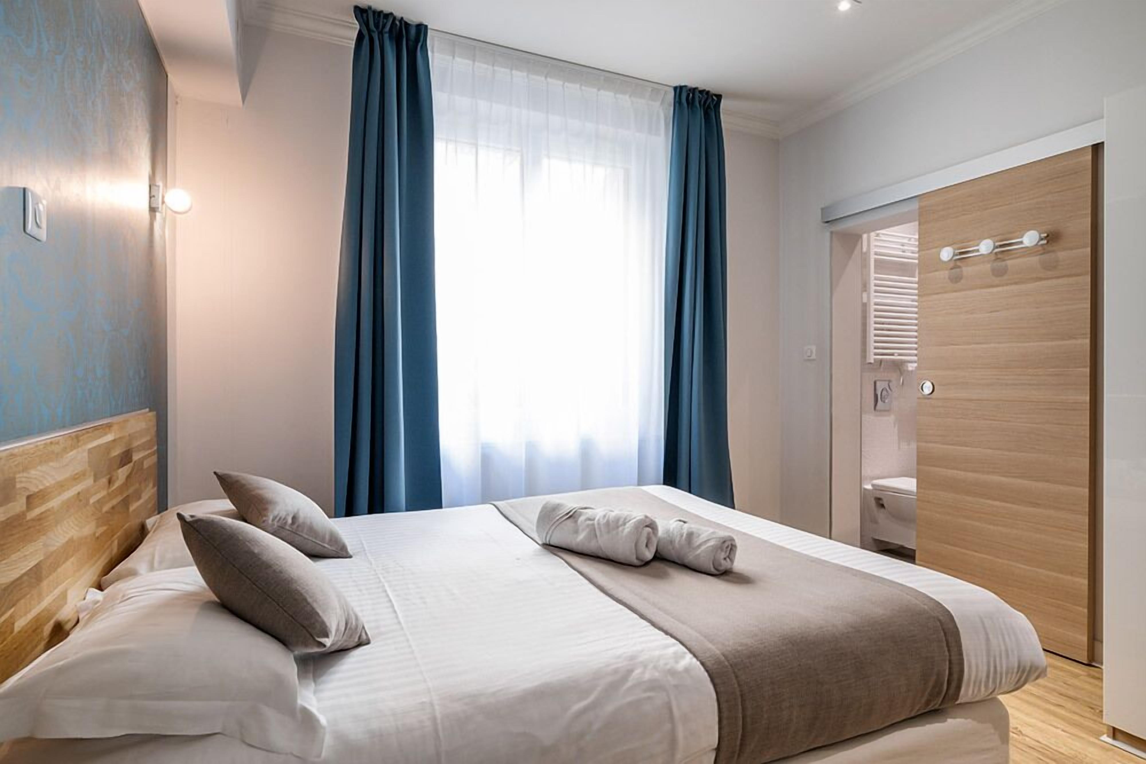 A hotel room with a bed, a wooden headboard, a wardrobe, and a bathroom visible through an open door.