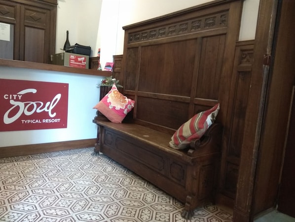 Una banca de fusta amb coixins decoratius, un cartell que diu "City Soul Typical Resort" i terres de rajoles amb disseny.