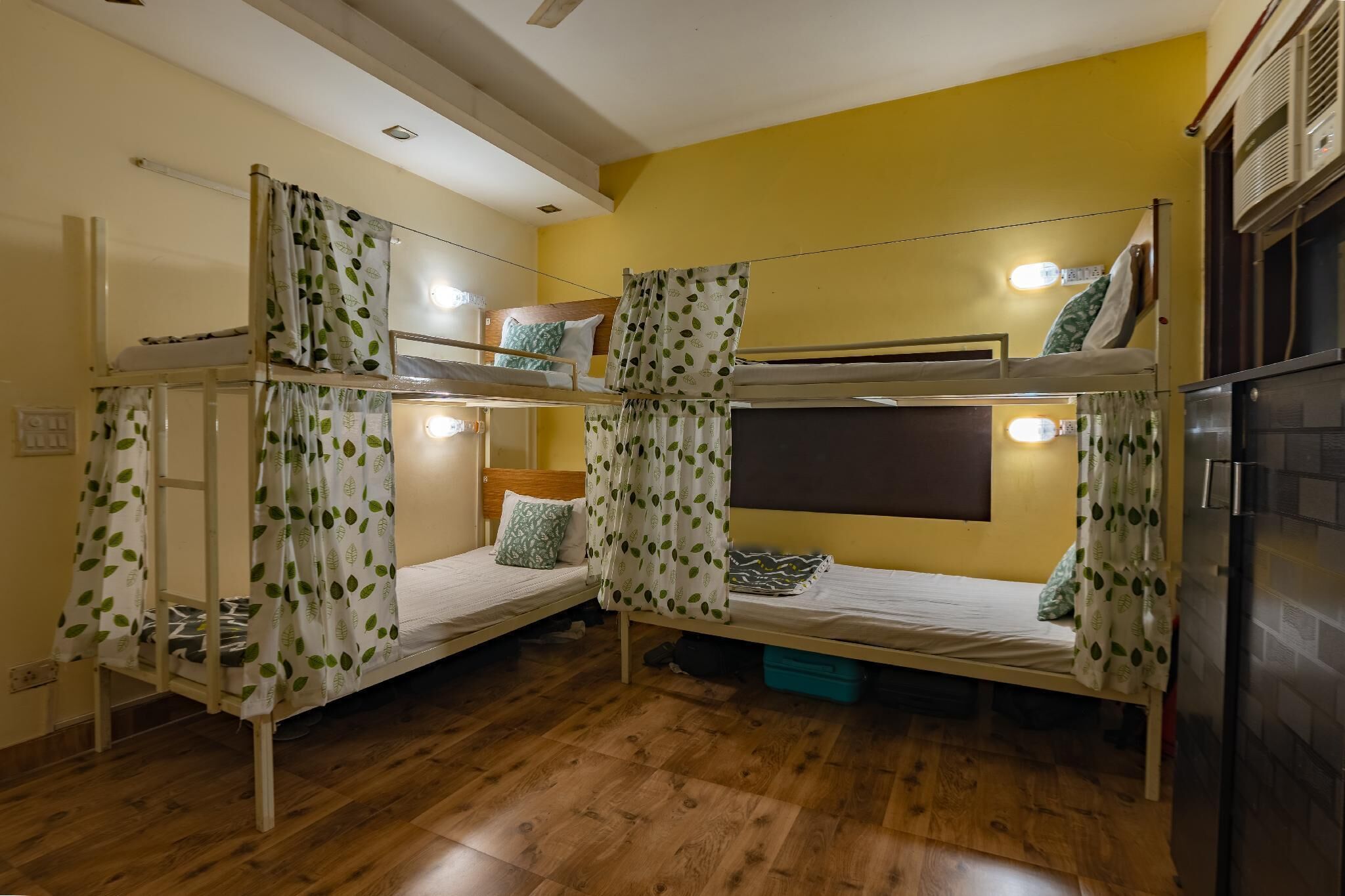 A dormitory room with bunk beds, wooden flooring, and a yellow wall.