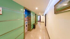 A hotel hallway with green walls, a framed landscape painting, and a tiled floor.