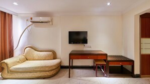 A room with a sofa, a table, a TV, and an air conditioning unit.